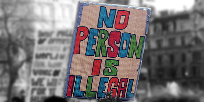 A close up of a sign at a protest which reads, 'no person is illegal'. The sign is in colour whilst the background is black and white.