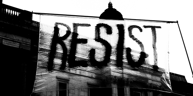 Black and white photo of a banner at a protest which reads, 'resist'.